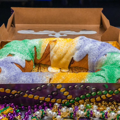 A whole Gambino's traditional king cake, iced in purple, green, and gold, ready to be sliced and shared.