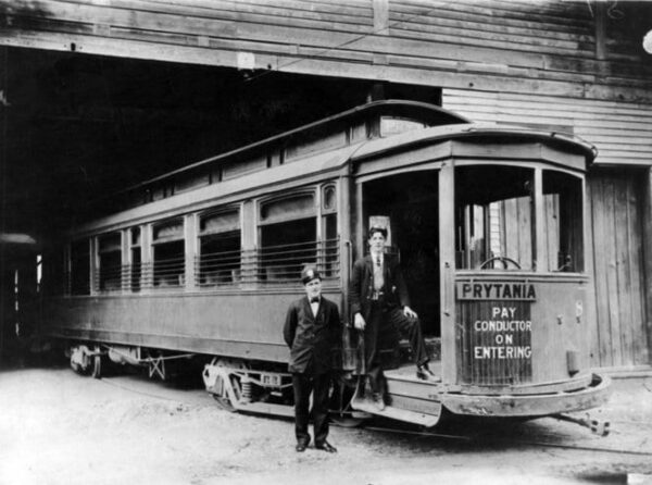 Prytania streetcar line, 1907. Two uniformed men stand by streetcar entrance, presumably the motorman and the conductor. Streetcar is at a carbarn, likely the Prytania barn. Courtesy of Wikipedia.