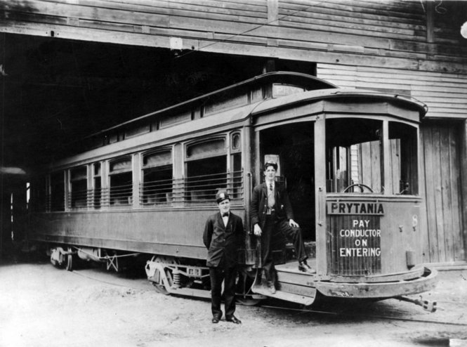 Prytania streetcar line, 1907. Two uniformed men stand by streetcar entrance, presumably the motorman and the conductor. Streetcar is at a carbarn, likely the Prytania barn. Courtesy of Wikipedia.